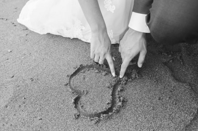 bride and groom drawing a heart shape on the sand